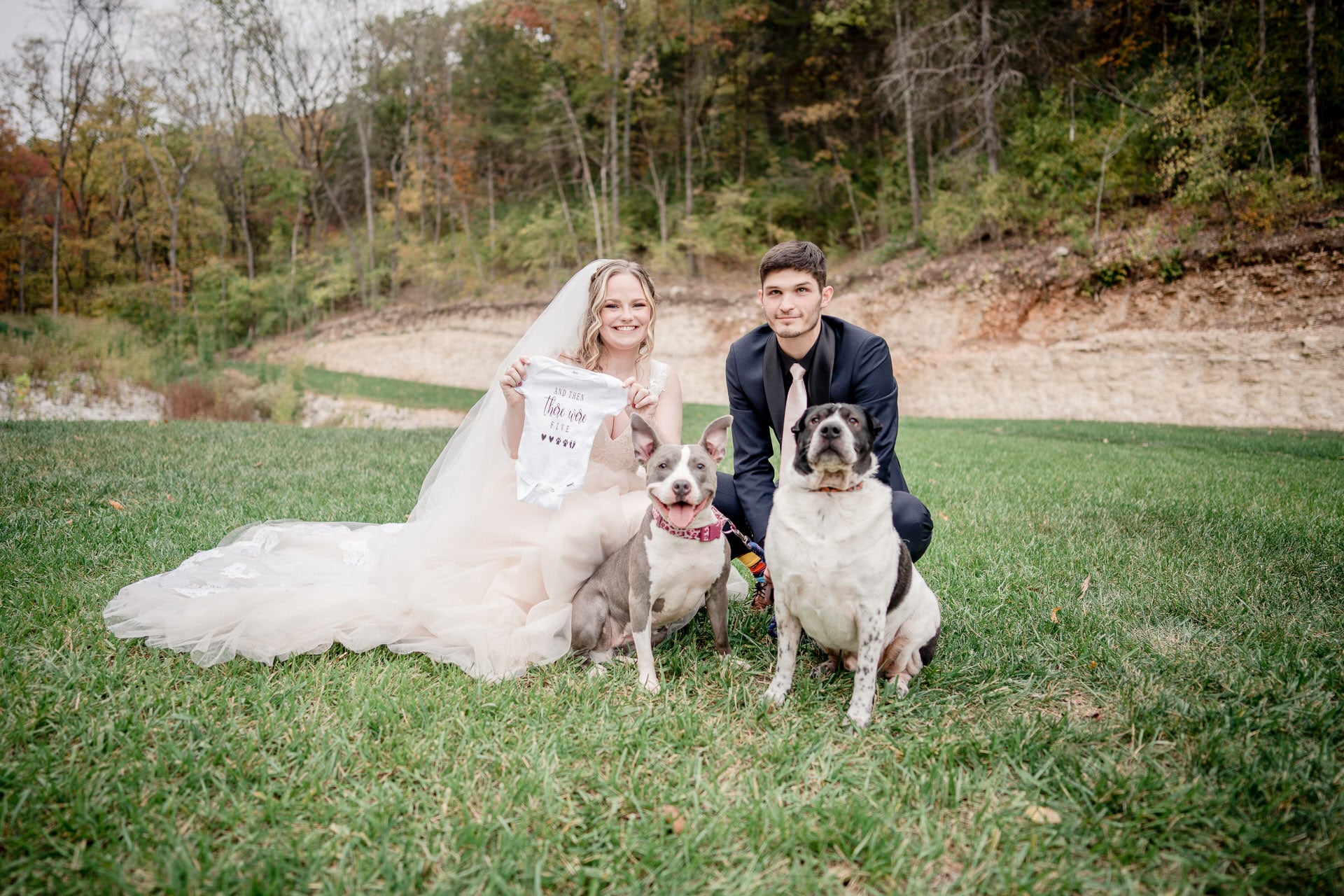 Bride and groom kneeling with their two dogs in a grassy field at Pine Hollow Farms Wedding Venue in Eureka, Missouri
