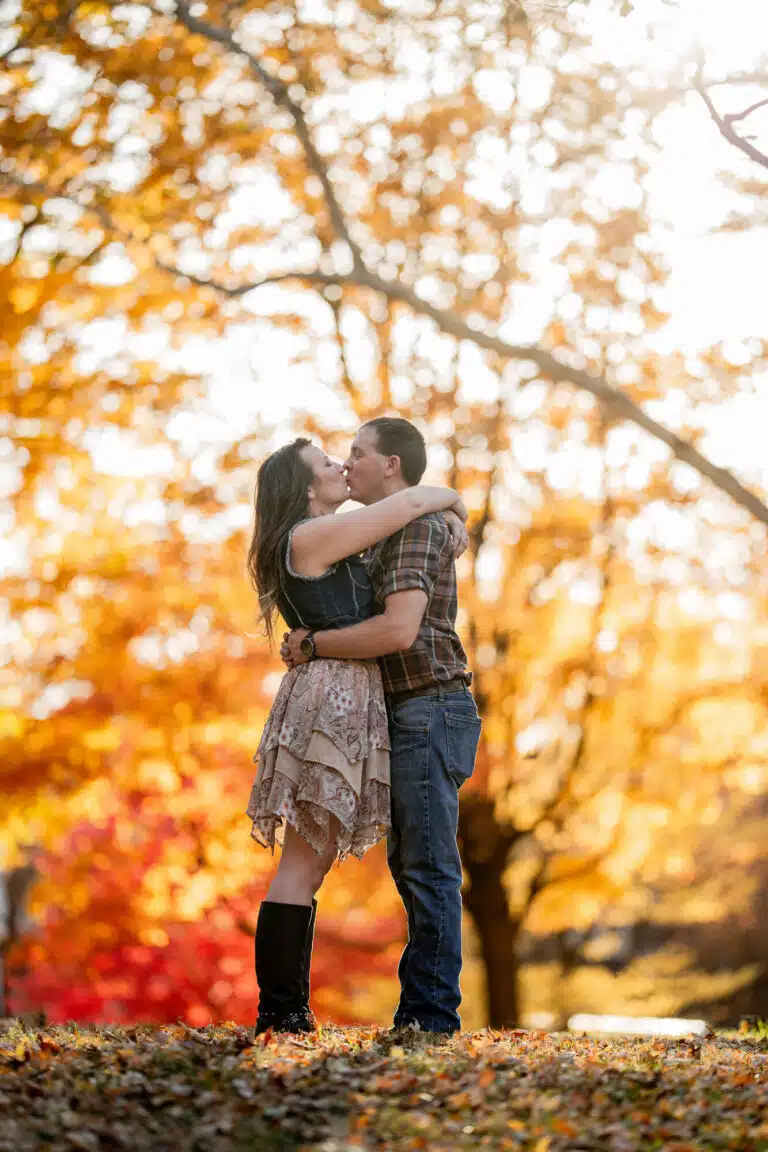 Couple kissing under backlit gold and orange leaves during a fall engagement session at Lafayette Park in St. Louis